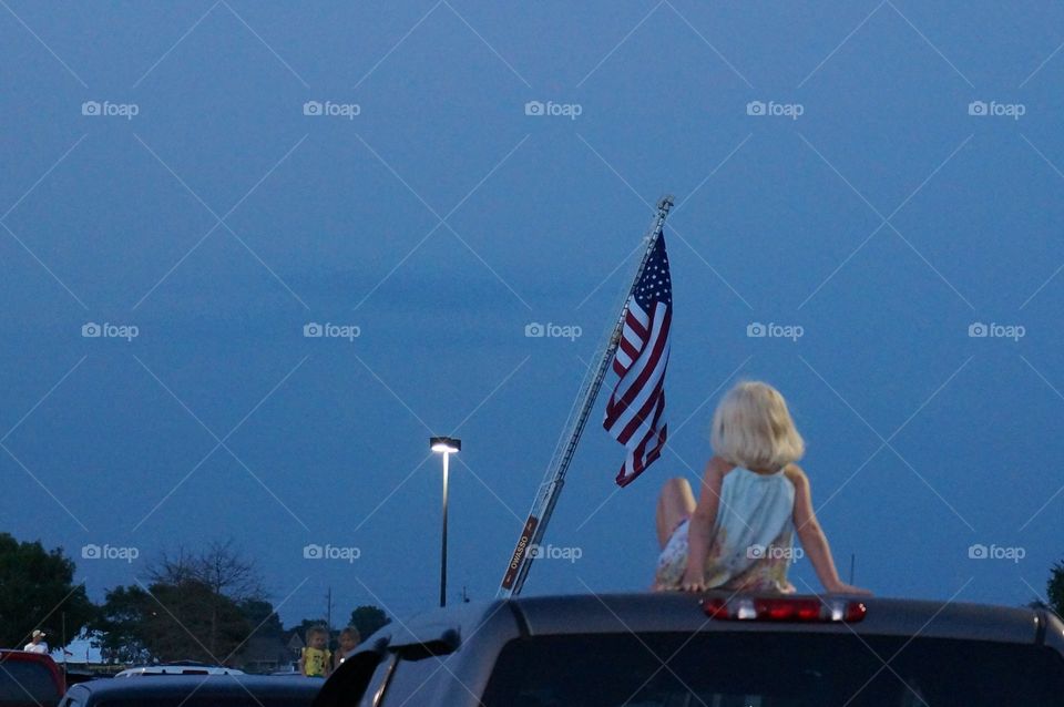 Girl on truck for fireworks . Photo taken in Owasso, OK. Girl on truck to watch fireworks. fire department has large U.S. Flagging on extended ladder.