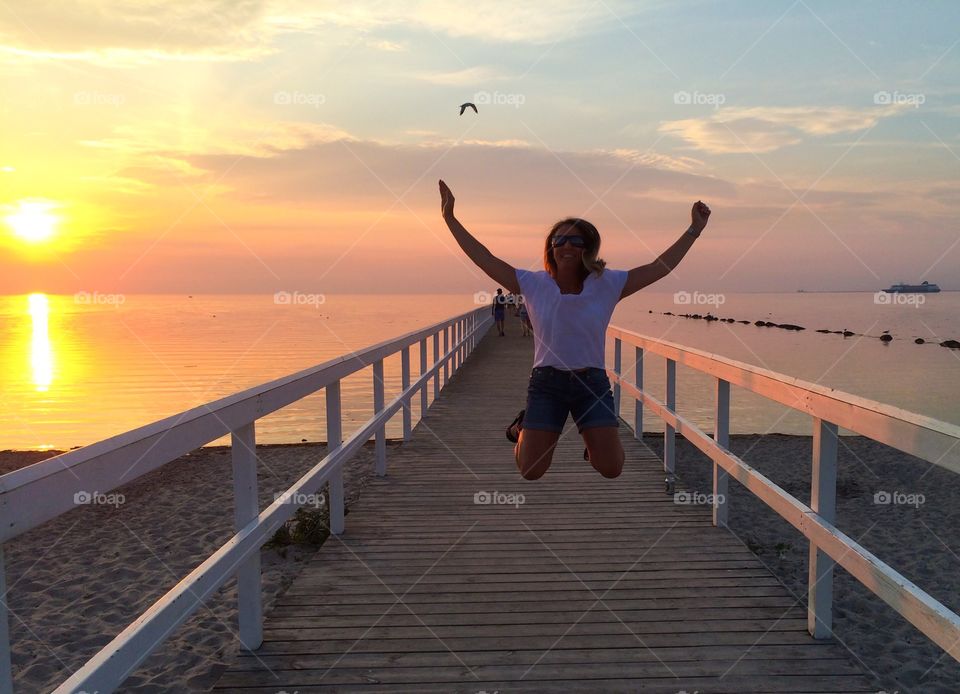 Woman jumping on pier at beach in the evening