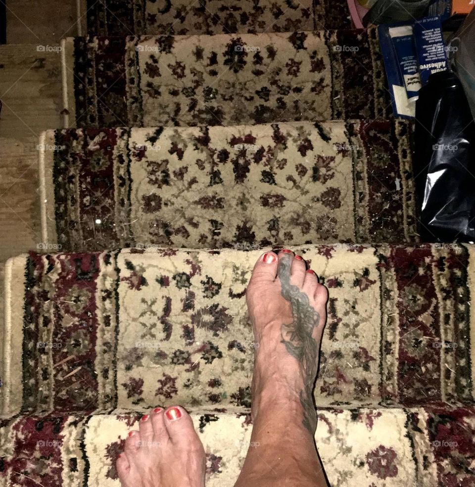 There is a girl stepping down a flight of stairs bare footed. She has a tattoo on her foot and her toe nails are painted with nail polish.