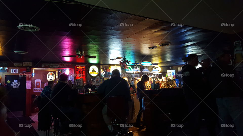 Colorful bar lights reflect an abstract design in the darkness and silhouette patrons.