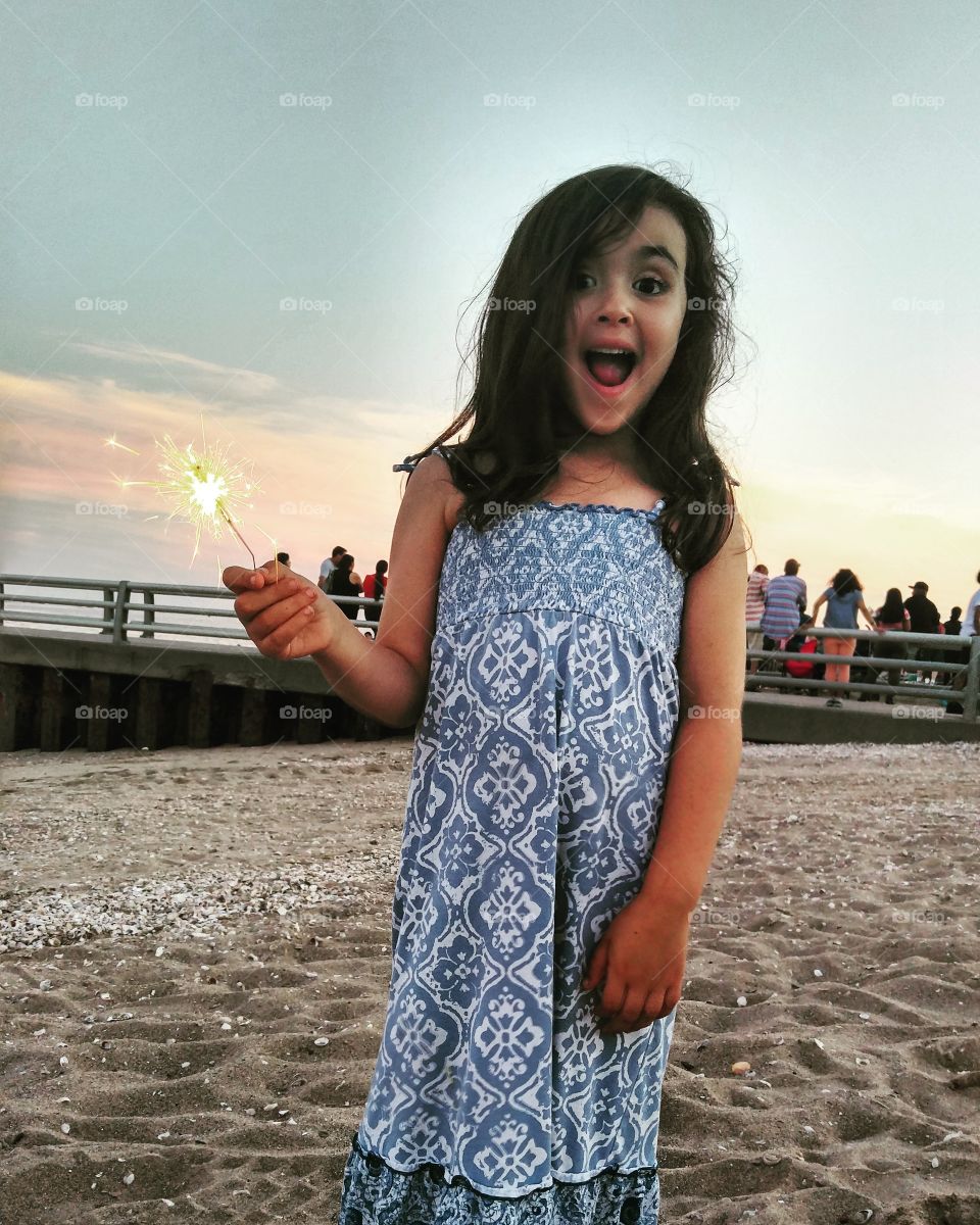 Cute little girl holding sparkler in hand at beach