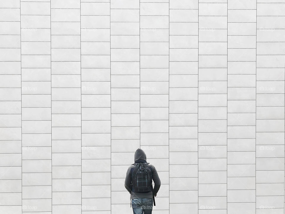 Young man with a backpack traveling through the city on urban geometric wall background 