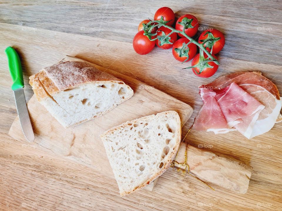 wooden cutting board with cherry tomato bread and raw ham sandwich