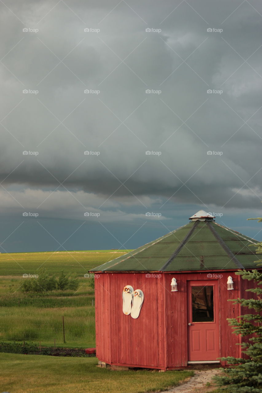 Red, wood, octagon farm building with flip flops decoration on side under stormy sky