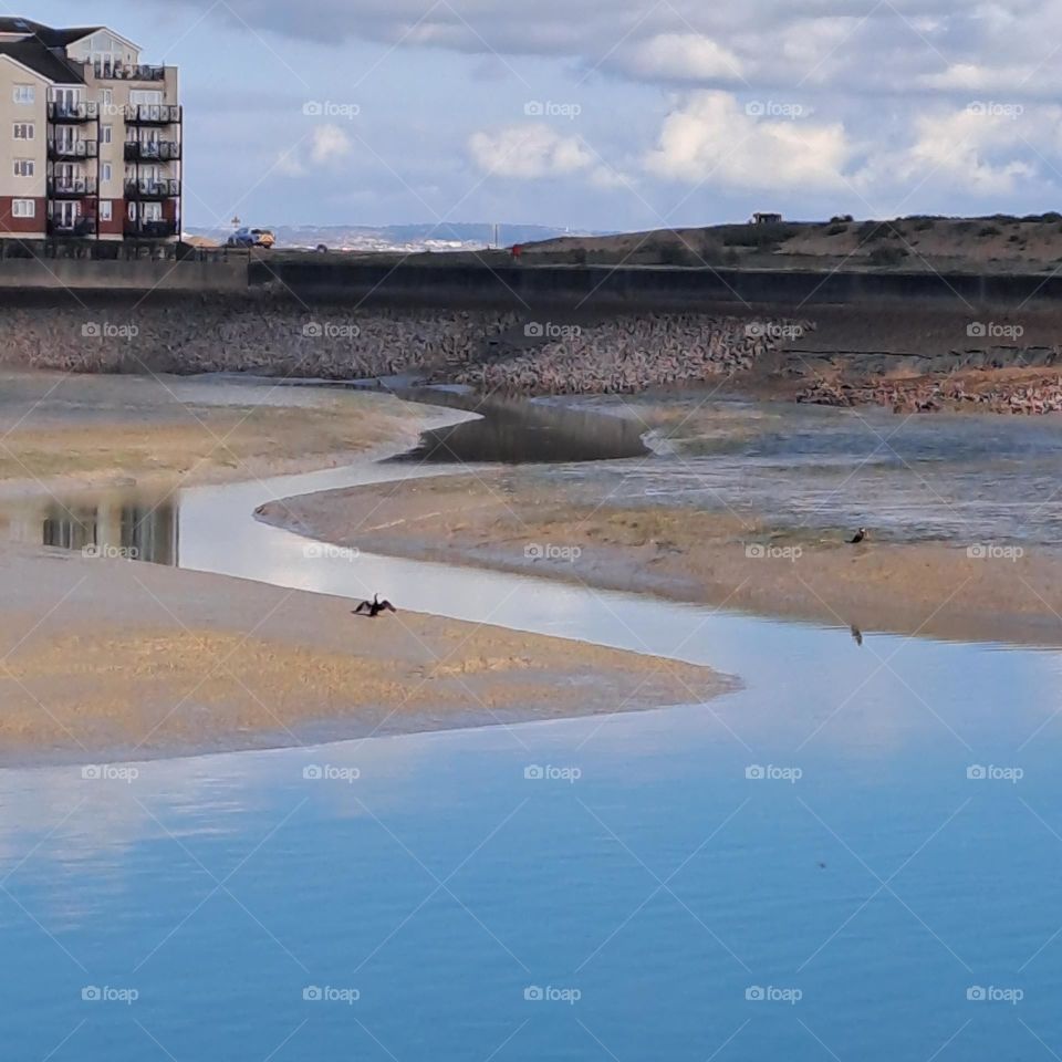 sea inlet, curved, sands reflection of nearby building, cloudy sky