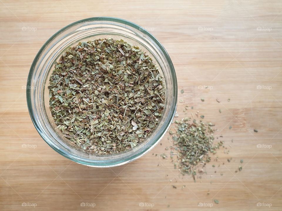 Dried oregano leaves, the famous mediterranean herbs in a glass jar on a wooden table. Top view Close up