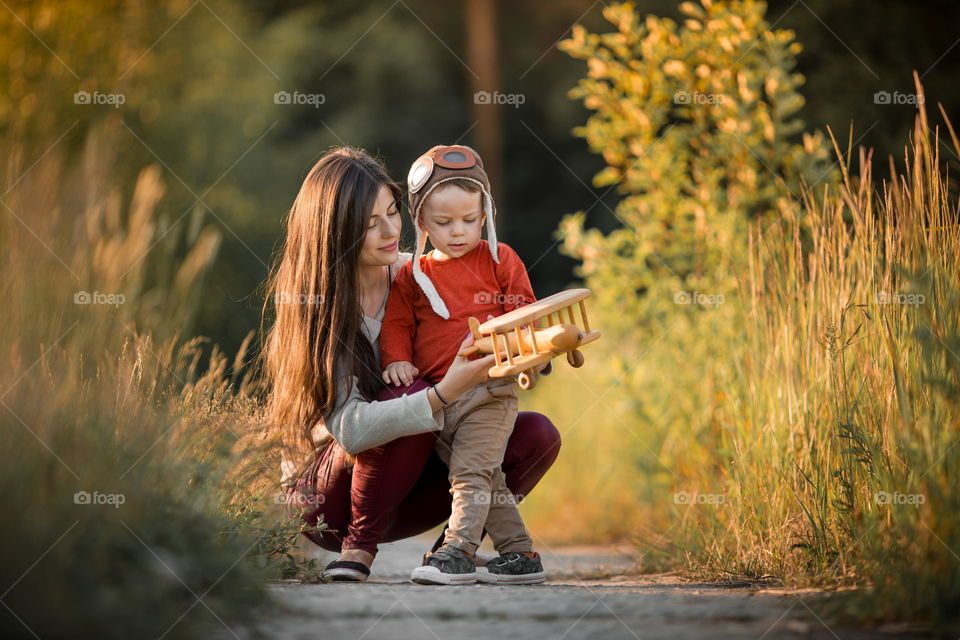 Mother with son playing with wooden plane at sunset