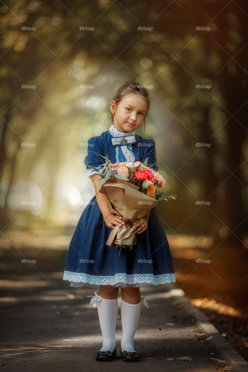 Little schoolgirl with a bouquet at a park 