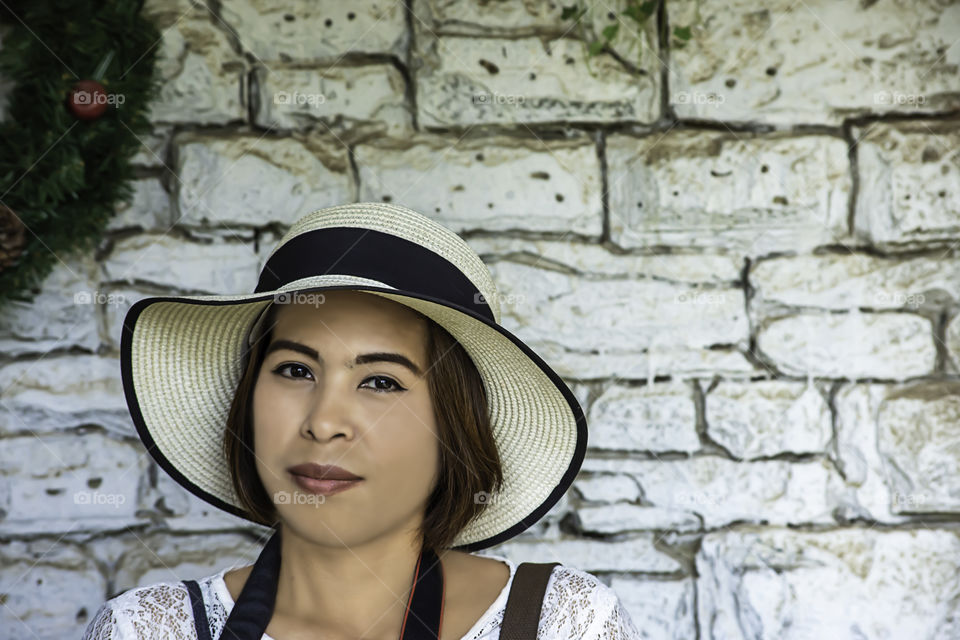 Portrait Asian woman with short hair wearing a hat with white brick wall background.