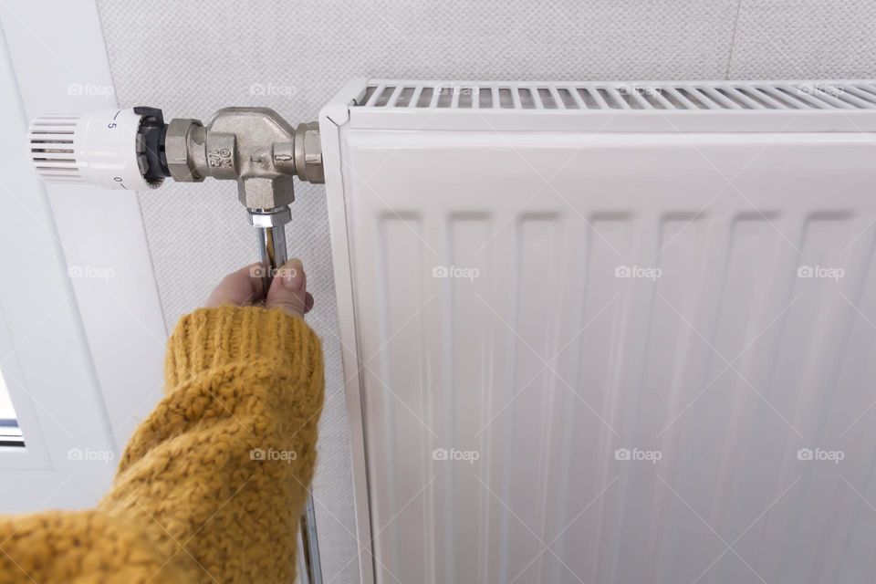 A woman's hand in a yellow sweater checks the heat on a heater with a thermostat..