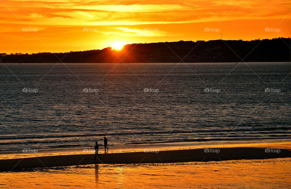 People walking on the beach at sunset.