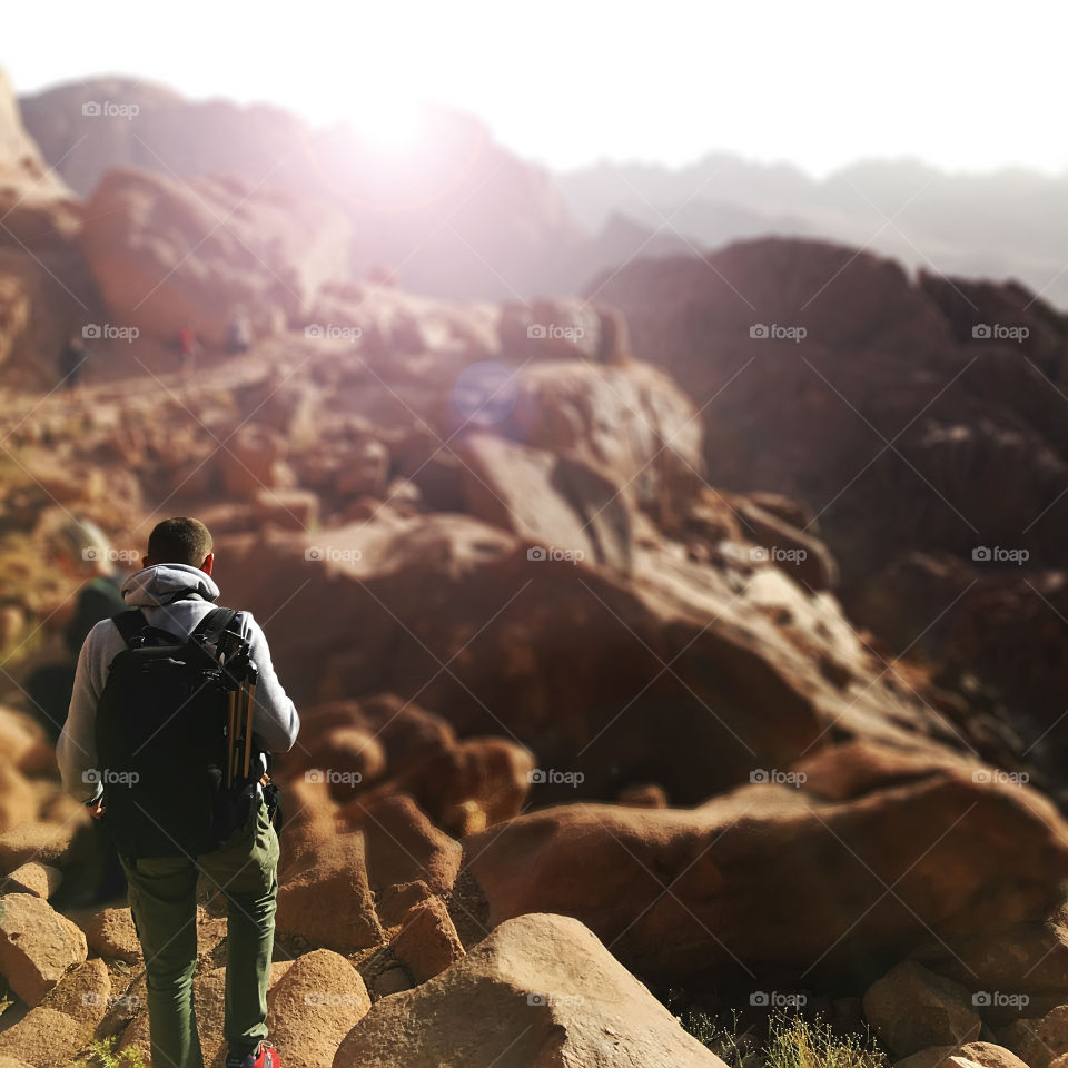 Young man hiking with a backpack by mountains at sunrise 