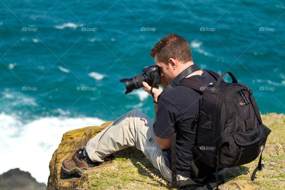 Relaxing by the sea and capturing the beautiful blue breaking waves - image of a man photographing the sea below