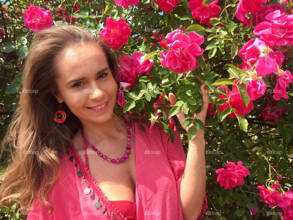 Portrait of young woman in pink surrounded by pink roses in the garden 