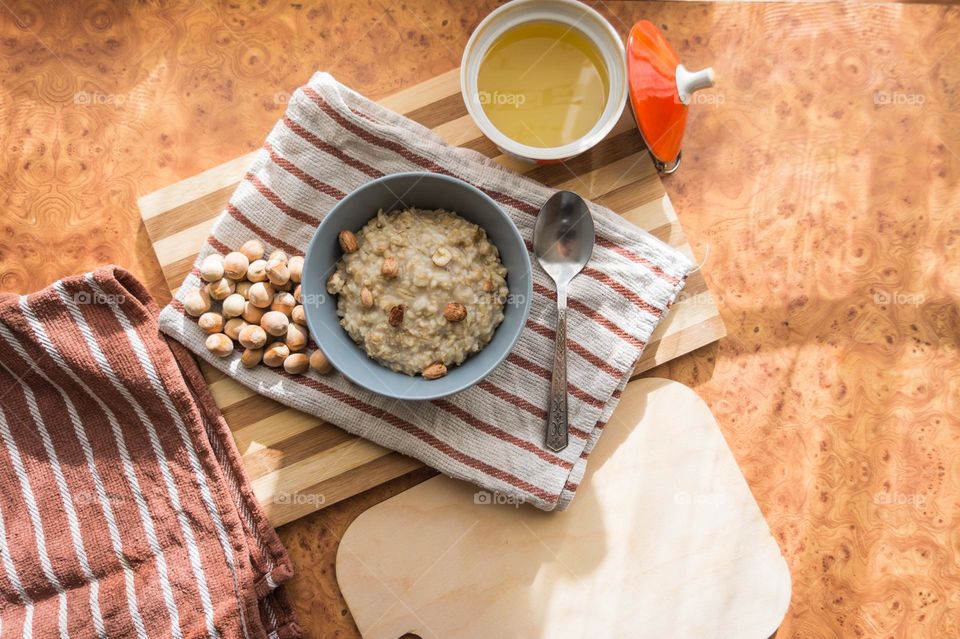 Cooked oatmeal in a deep gray plate with hazelnuts and honey.