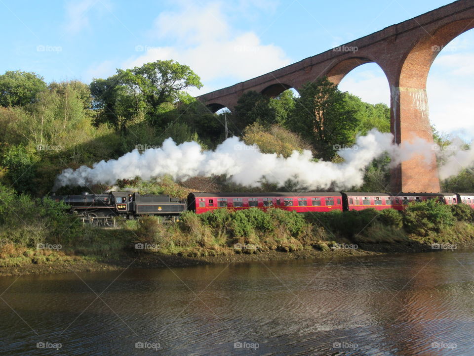 Steam train going under whitby viaduct with the river esk next to railway line