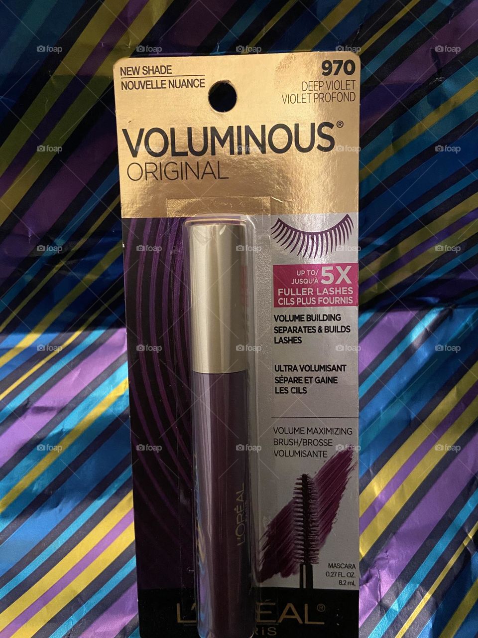 L’Oréal Voluminous Mascara in Deep Violet against a shimmery striped background in various jewel tones that compliment the product nicely. 