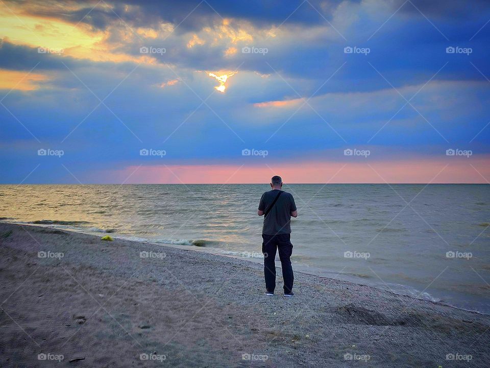 Summer.  Summer sunset on the sea.  Clear sea, warm sand.  A man stands on the shore and looks at the sea and the sunset.