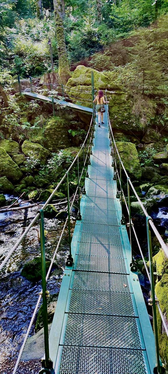The „Buchberger Leite“ is a place near the township of „Ringelai“ in „Bavaria“ where the river turned white water rapid „Ohe“ cut a valley 100 meters deep into the surrounding rocks. A hanging bridge leads across. 2023. Hypnotic Productions