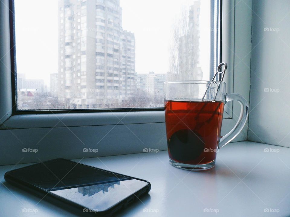 a cup of black tea and a smartphone lie on the windowsill