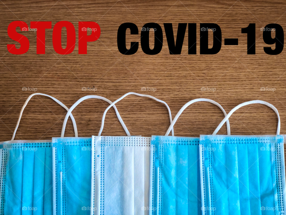 Multiple surgical masks on wooden table with the message to stop covid-19