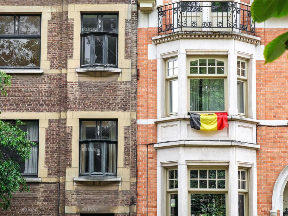 A beautiful view of the Belgian flag hanging from the window of the house on the second floor on a sunny summer day, side view close-up.