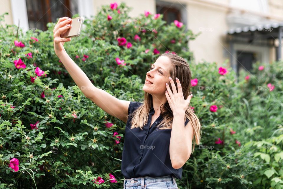 young beautiful girl in the park in spring holds a phone in her hands and takes a selfie