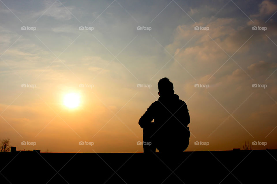 a man's sitting under sunset