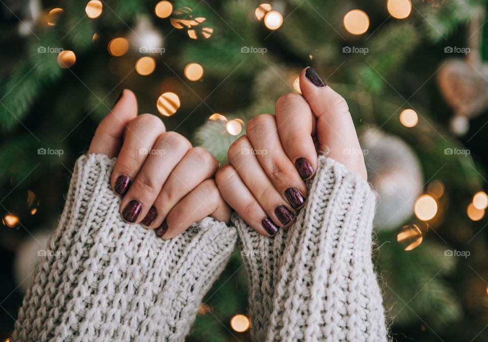 Close-up photo of female hands with painted nails in front of christmas tree