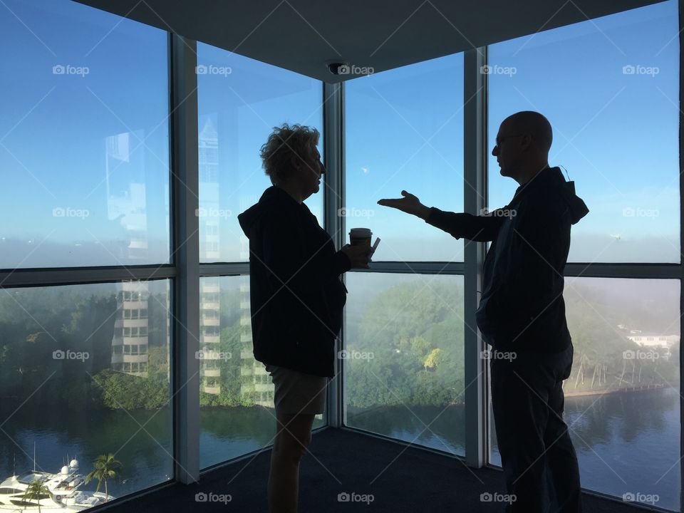 Man and woman standing by panoramic window in building, Miami Beach, Florida, USA 