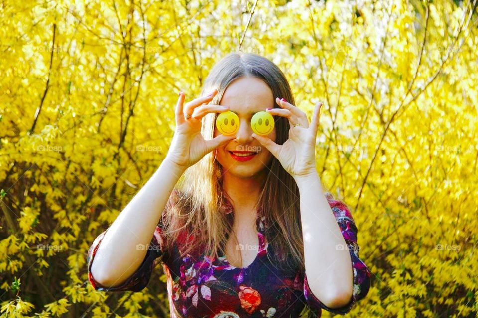 Woman with two smiley emoticons as her eyes standing against yellow flowers background