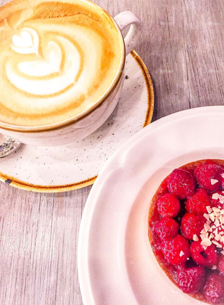 Cappuccino decorated cup and raspberry tart for breakfast in detail 