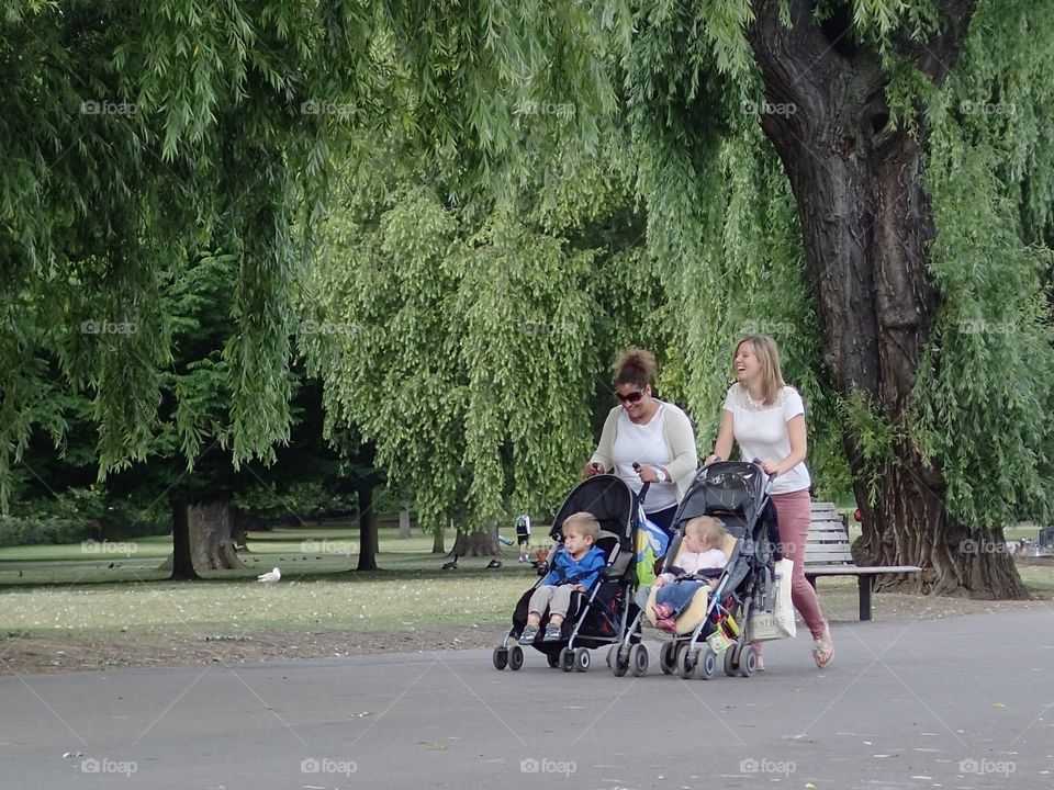 Two moms laughing and having a great time while taking their kids out in strollers on a summer day in Regents Park in London. 