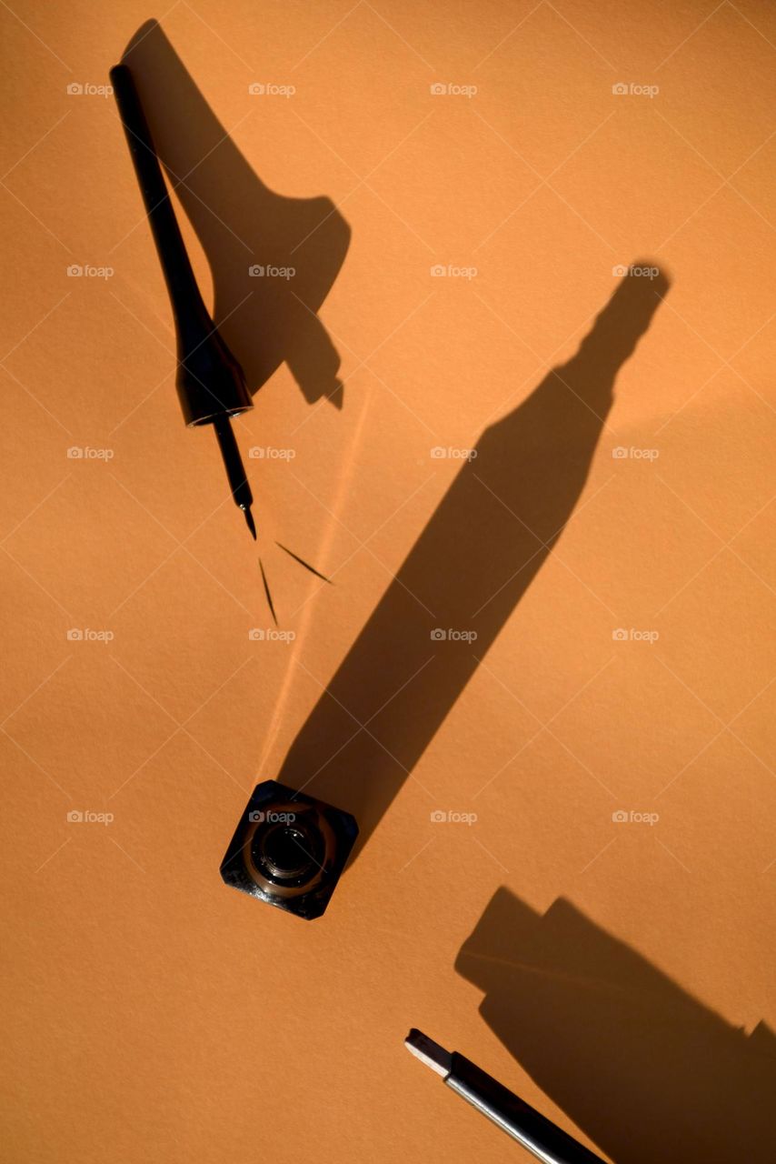 Black eyeliner and eyebrow pencil on an orange background.