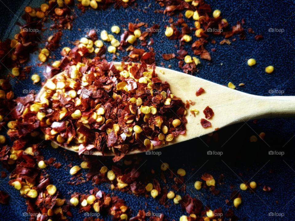 Dried red chili pepper flakes on wooden spoon.  Crushed chillies.