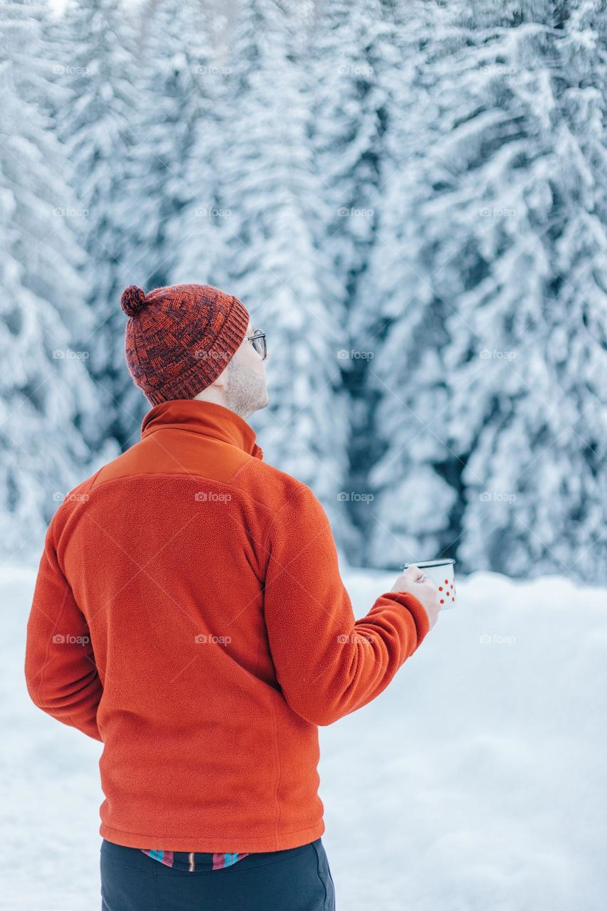 Man holding a cup of tea, while being in the mountains on a winter day.