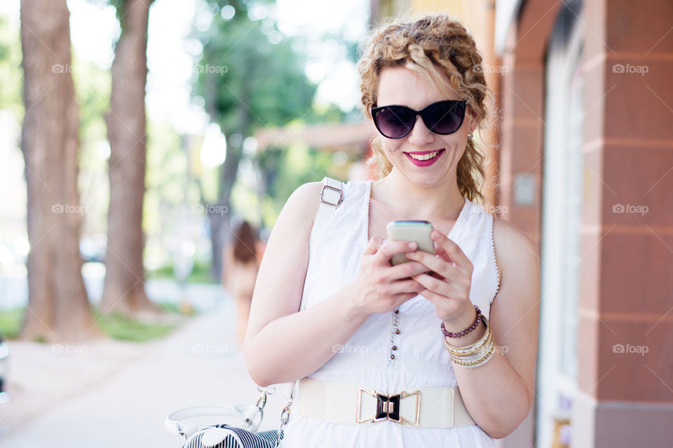 girl with sunglasses and phone. curly blond girl typing on the phone wearing sunglasses