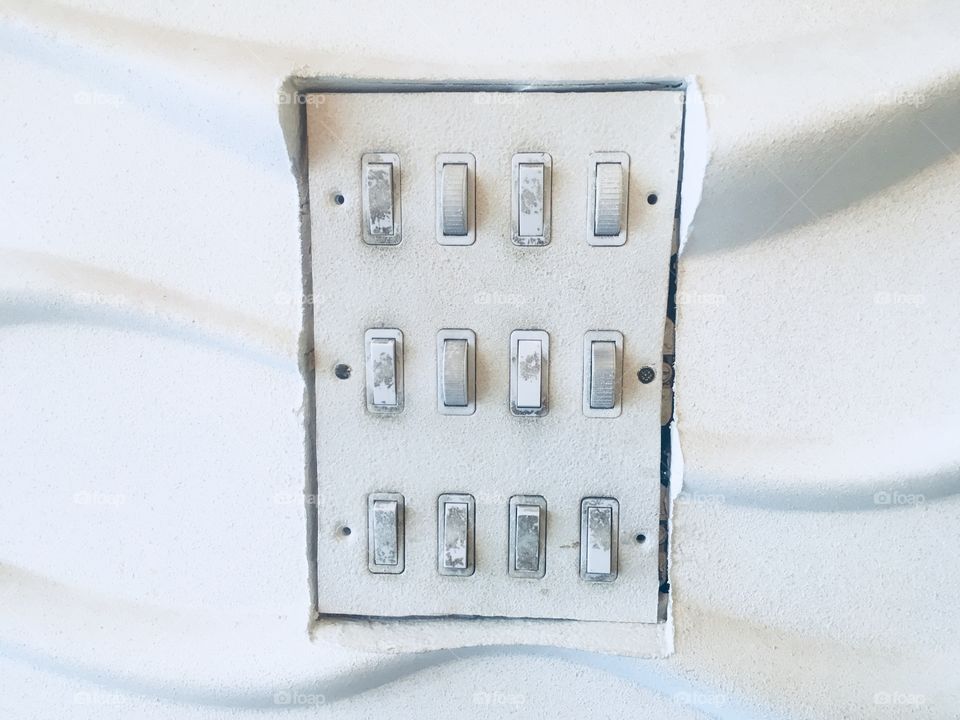 A dozen light switches on a textured wall at the Promised Land Cafe, Whetstone. Visited in Spring.