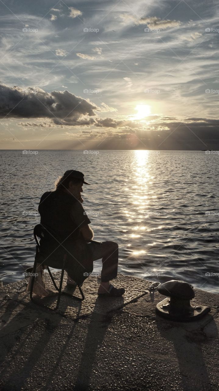 A silhouetted man sits at the dock of the bay in Rovinj, Croatia, at sunset