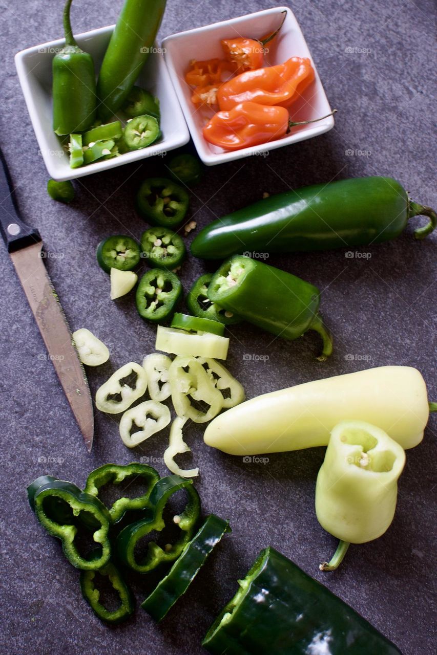 Variety of cut peppers and a knife on a slate background 