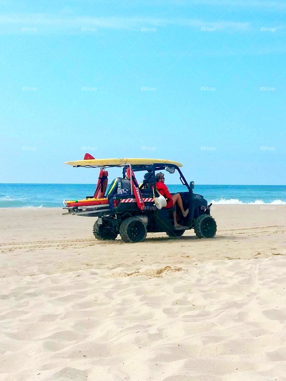 A sea rescue vehicle moves on the beach, equipped with lifebuoys, a surfboard and other rescue equipment. Lifeguards are ready to intervene to guarantee the safety of holidaymakers.