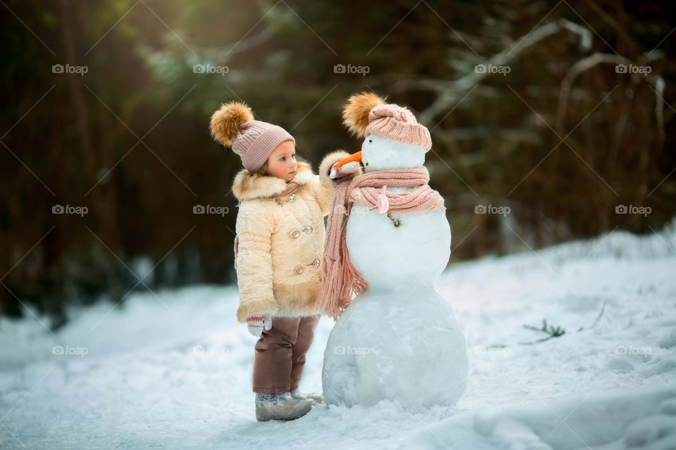 Little girl with snowman in winter forest at sunny day