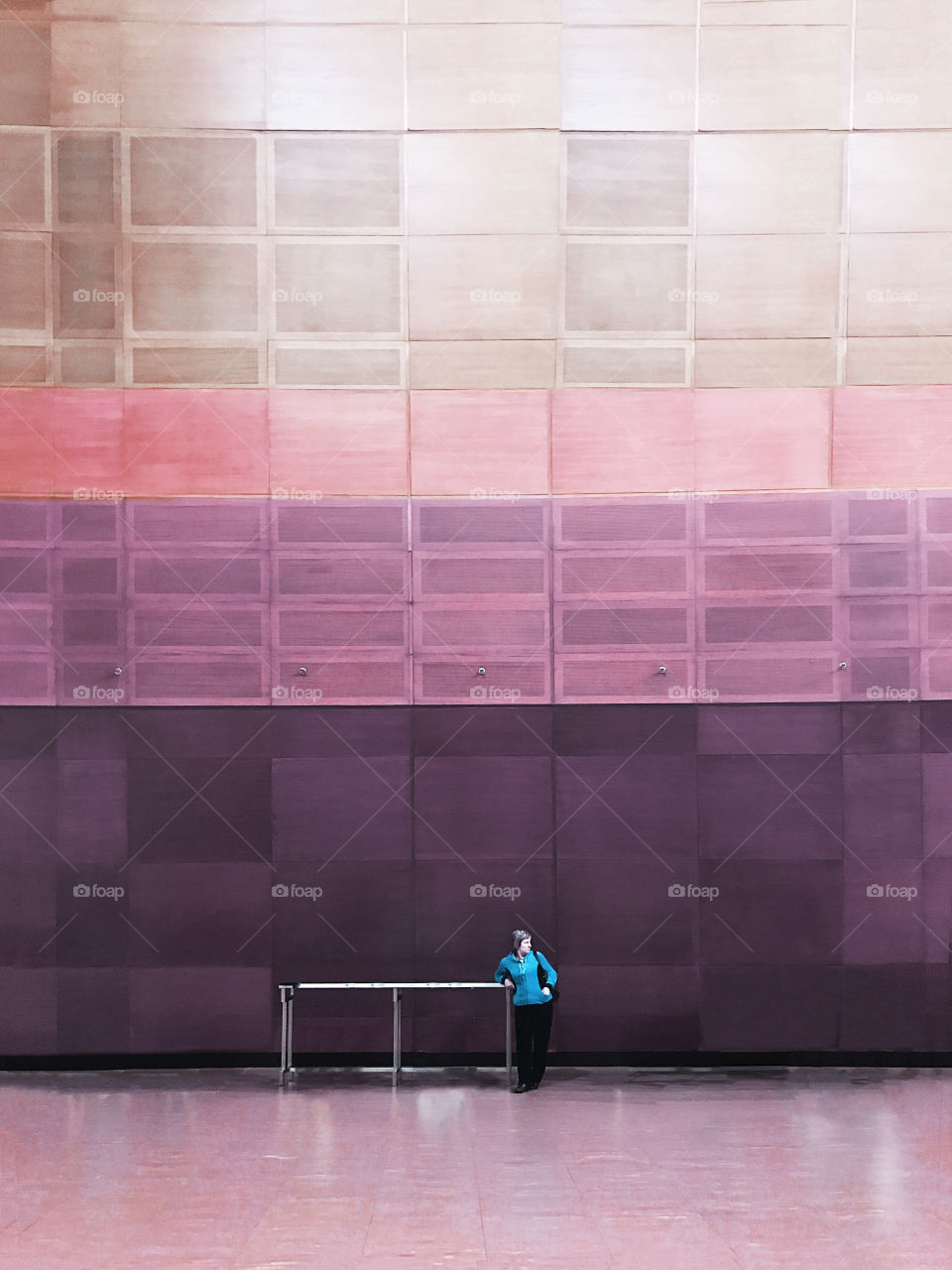 Tiny figure of a Woman standing in front of huge geometric wall background 
