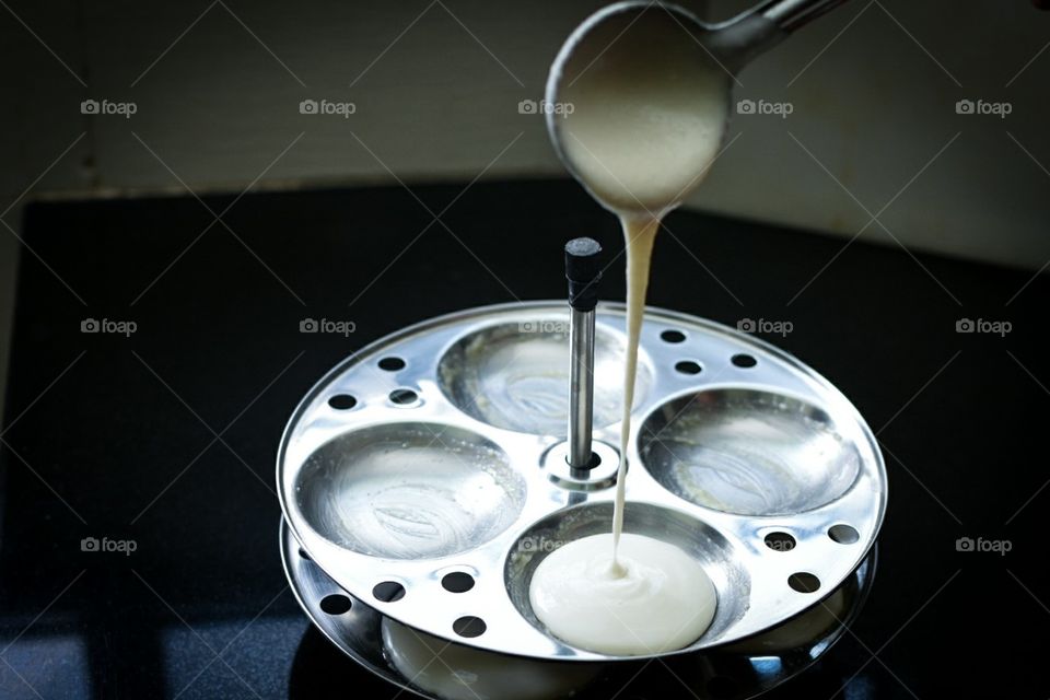 Indian idli batter poured into trays using a ladle into circular trays for Indian Idli (Idly / rice cake) by steaming