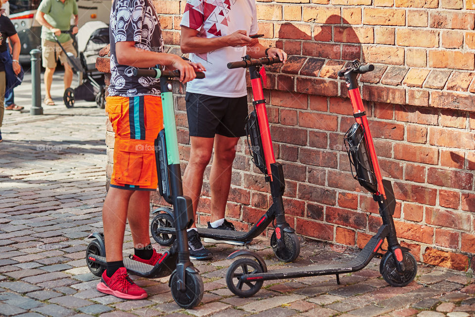 Two men hiring electric scooters using rent service on smartphone. Candid people, real moments, authentic situations