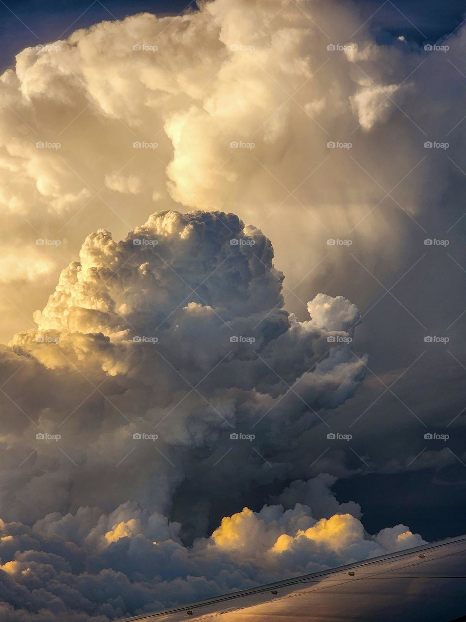 A beautiful powerful storm cloud glows with the setting sun as photographed through a Boeing 737 window at 30,000 feet