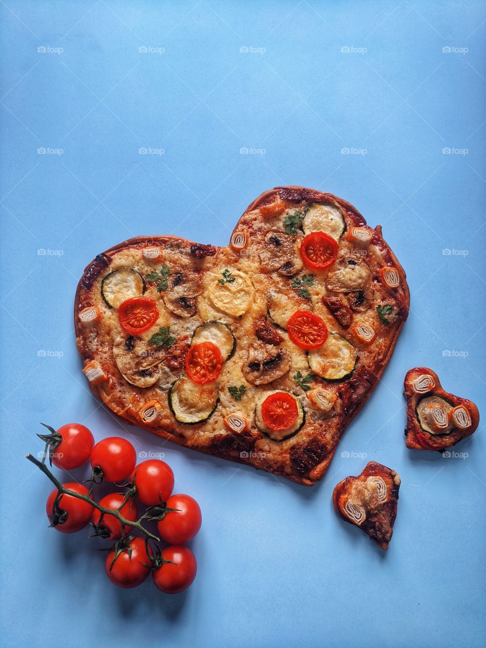 Delicious vegetarian pizza in the shape of a heart for Valentine's Day with tomatoes, vegetables and cheese on a blue background.