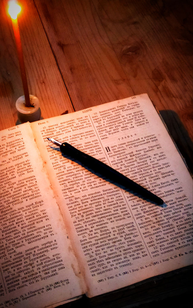 Antique Bible, with a quill pen and a church candle that burns