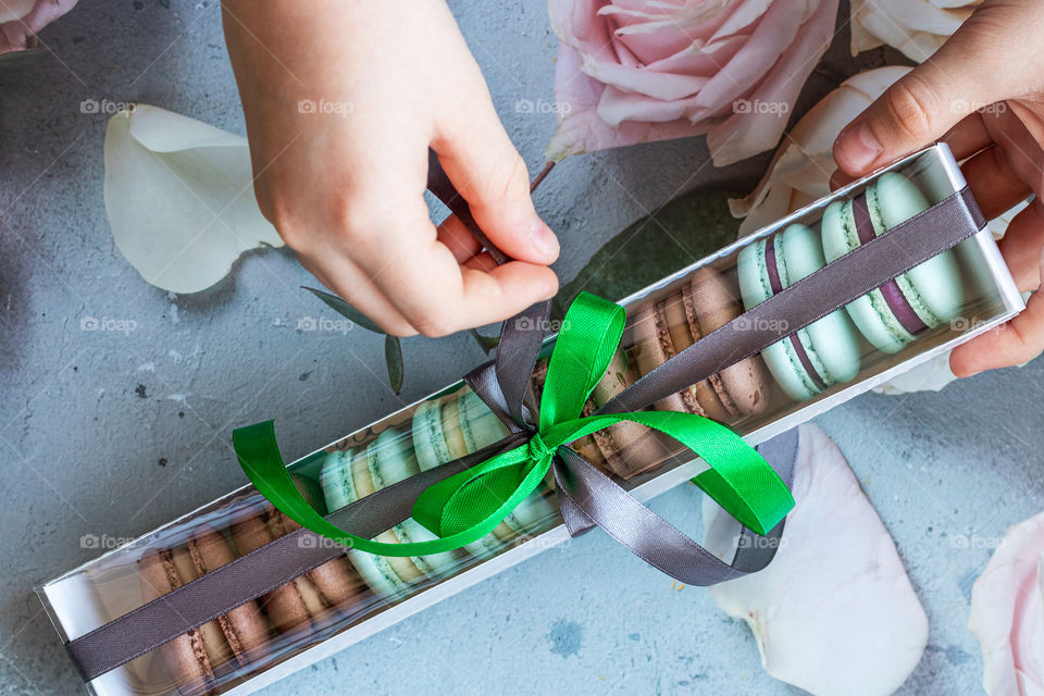 Hands take a festive box with assortment of macarons on floral background. Perfect gift.