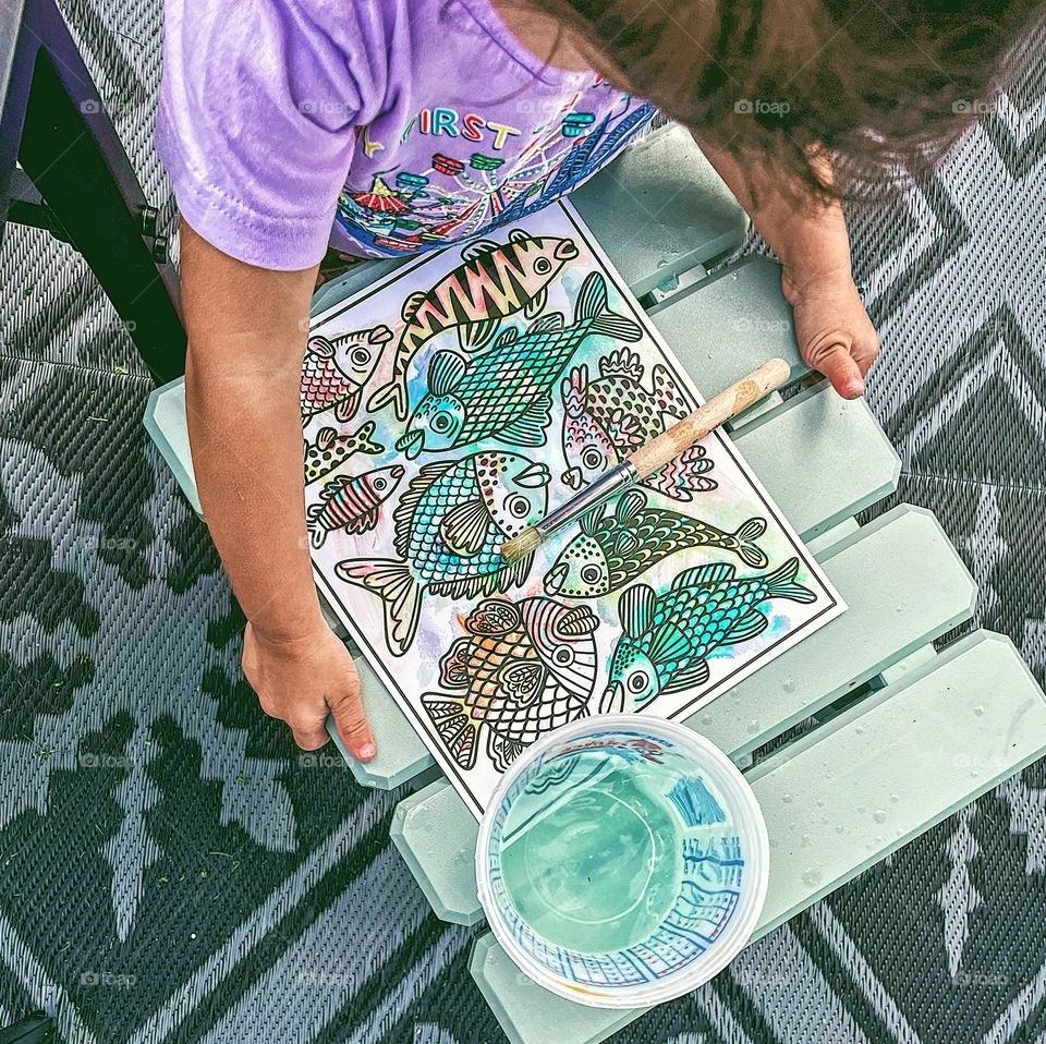 Little girl looking at her art project, toddler with art project, toddler painting fish outside, toddler and fish, toddler girl doing crafts 